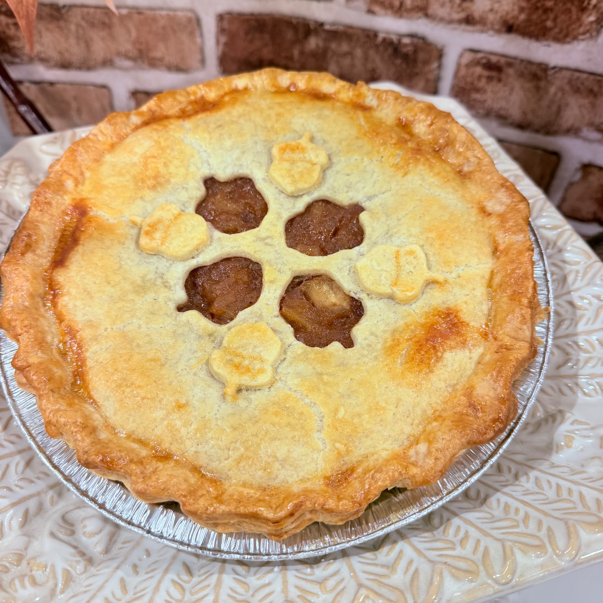 Golden double-crust apple pie with acorn pastry cutouts on a white leaf-pattern platter — Thanksgiving pies baked to order by Mama Rozi's Bakehouse in LaGrange, KY